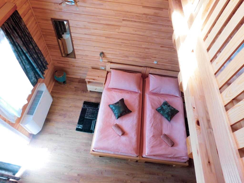 A king size bed with pink covers and pink pillows. All in a wooden room with the AC in the left corner.