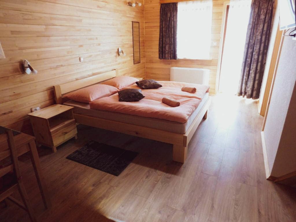 Two bed side by side with blue pillows on top of them. The walls in this room are made out of wood with a blue table sat beside them.