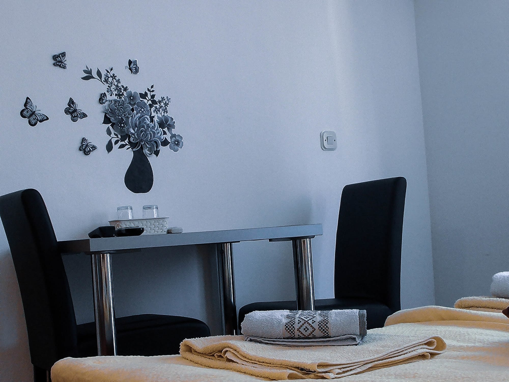 There is a gray table with two black chairs next to it. They are all next to a white wall with gray flowers painted on it.